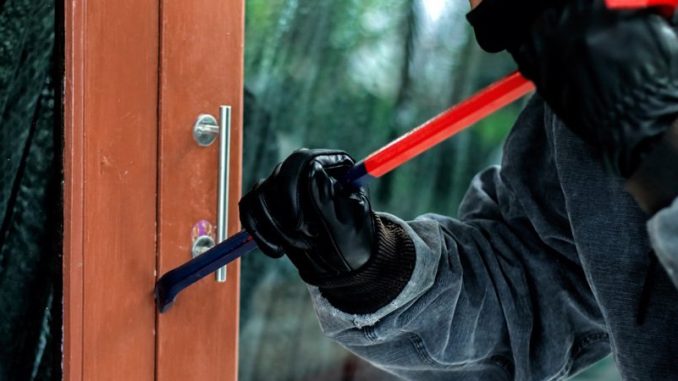 Burglar with crowbar trying break the door to enter the house
